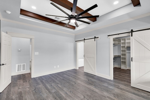 unfurnished bedroom featuring a barn door, ceiling fan, dark hardwood / wood-style flooring, and a walk in closet