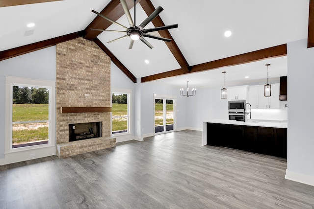 unfurnished living room with ceiling fan, sink, a brick fireplace, beamed ceiling, and light hardwood / wood-style floors