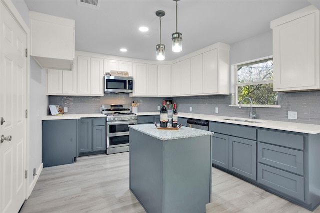 kitchen with sink, appliances with stainless steel finishes, white cabinetry, a kitchen island, and decorative light fixtures