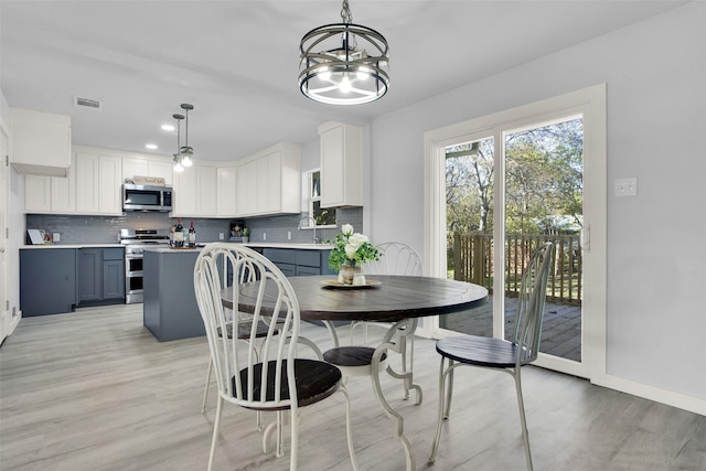 dining space with sink, light hardwood / wood-style floors, and a notable chandelier