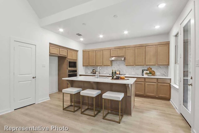 kitchen with appliances with stainless steel finishes, sink, light hardwood / wood-style flooring, and an island with sink