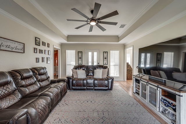 living room with light hardwood / wood-style floors, a tray ceiling, ornamental molding, and ceiling fan