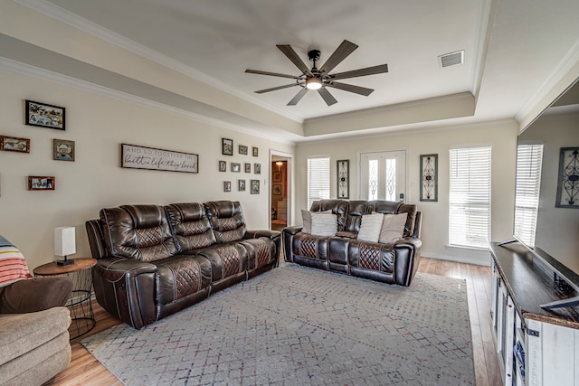 living room with light wood-type flooring, ceiling fan, a raised ceiling, and ornamental molding