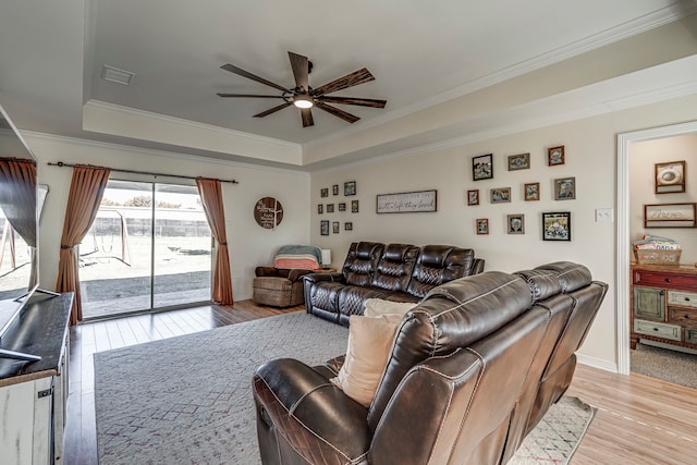 living room with ceiling fan, light hardwood / wood-style flooring, a raised ceiling, and ornamental molding