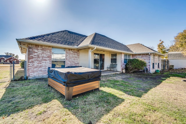 rear view of house with a hot tub, a lawn, and a patio