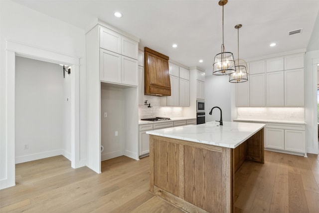 kitchen with white cabinetry, a center island with sink, light hardwood / wood-style floors, and appliances with stainless steel finishes