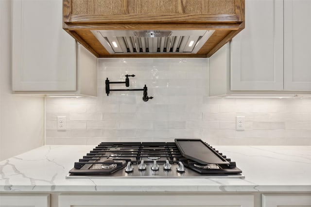 room details with stainless steel gas cooktop, tasteful backsplash, light stone counters, white cabinets, and custom exhaust hood