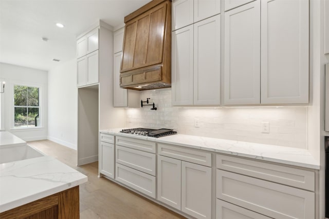 kitchen featuring premium range hood, white cabinets, light wood-type flooring, tasteful backsplash, and stainless steel gas cooktop