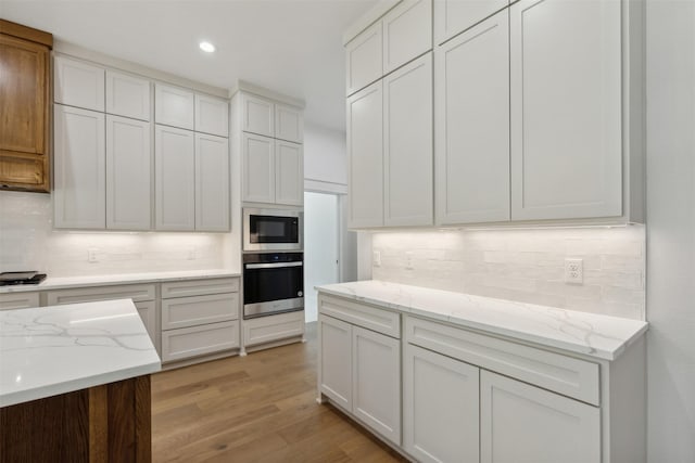 kitchen featuring light hardwood / wood-style flooring, light stone countertops, appliances with stainless steel finishes, tasteful backsplash, and white cabinetry