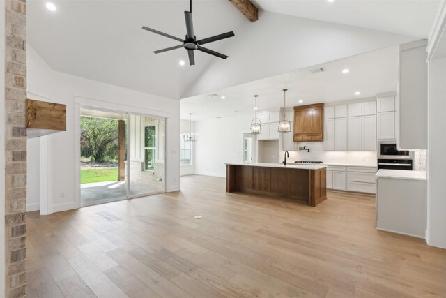 kitchen with white cabinets, high vaulted ceiling, a center island with sink, and light hardwood / wood-style flooring