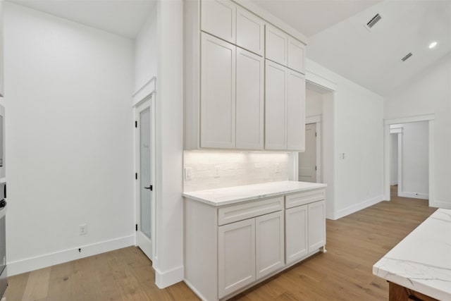 kitchen featuring light wood-type flooring, tasteful backsplash, light stone counters, vaulted ceiling, and white cabinets