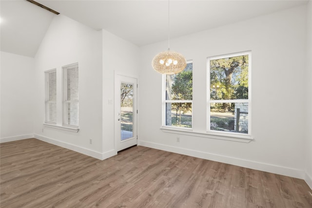 unfurnished dining area featuring wood-type flooring, lofted ceiling, and an inviting chandelier