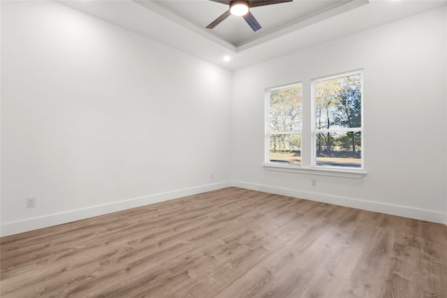 empty room featuring light hardwood / wood-style flooring, a raised ceiling, and ceiling fan