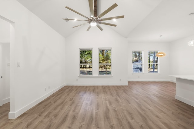 unfurnished living room with ceiling fan with notable chandelier, a healthy amount of sunlight, light hardwood / wood-style floors, and high vaulted ceiling