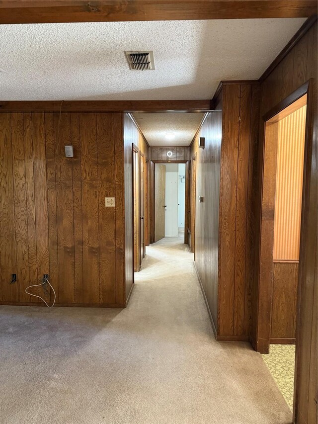 hall featuring a textured ceiling, light carpet, and wood walls