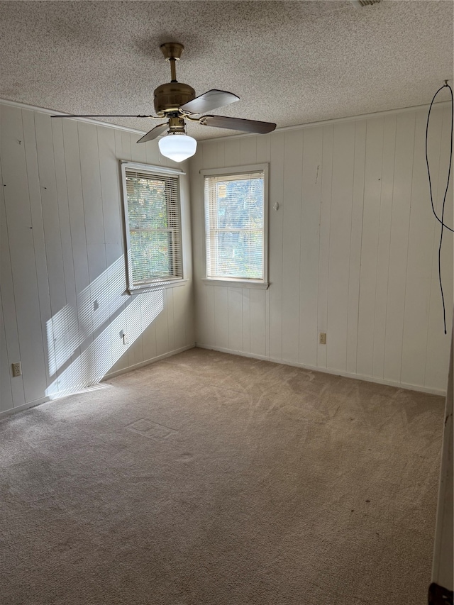 carpeted empty room with wooden walls, ceiling fan, and a textured ceiling