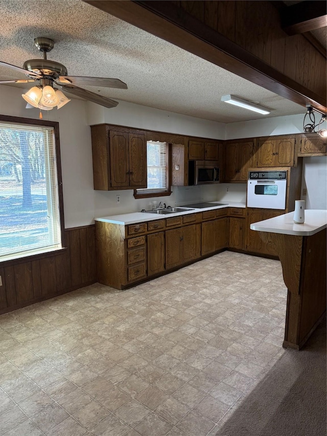 kitchen with dark brown cabinets, oven, a wealth of natural light, and wood walls