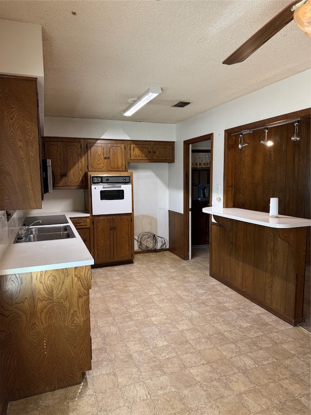 kitchen with kitchen peninsula, a textured ceiling, oven, and sink