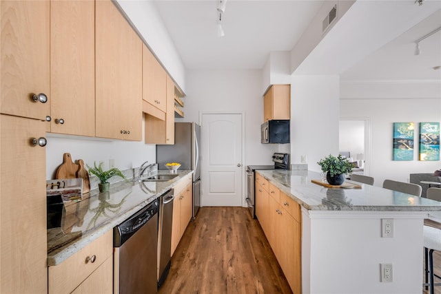 kitchen with appliances with stainless steel finishes, sink, a kitchen bar, light stone countertops, and light brown cabinets