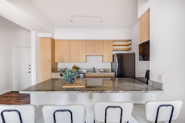 kitchen with light brown cabinetry, stainless steel refrigerator, sink, a kitchen breakfast bar, and kitchen peninsula