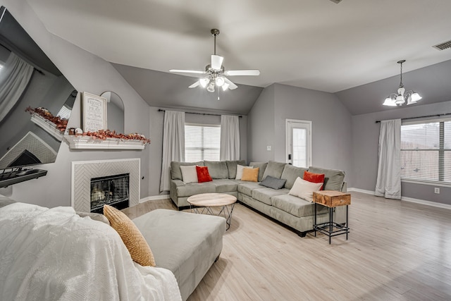 living room with light wood-type flooring, a tiled fireplace, vaulted ceiling, and a healthy amount of sunlight