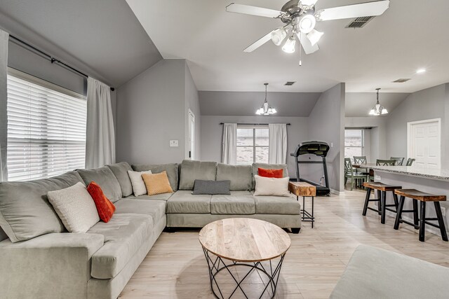 living room featuring ceiling fan with notable chandelier, light hardwood / wood-style floors, and vaulted ceiling