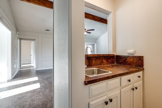 kitchen with lofted ceiling, white cabinets, sink, ceiling fan, and a textured ceiling