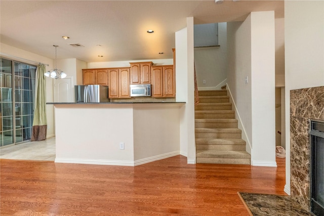 kitchen with hanging light fixtures, a high end fireplace, a notable chandelier, appliances with stainless steel finishes, and light wood-type flooring