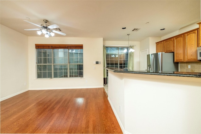 kitchen featuring decorative backsplash, ceiling fan with notable chandelier, wood-type flooring, decorative light fixtures, and stainless steel fridge with ice dispenser