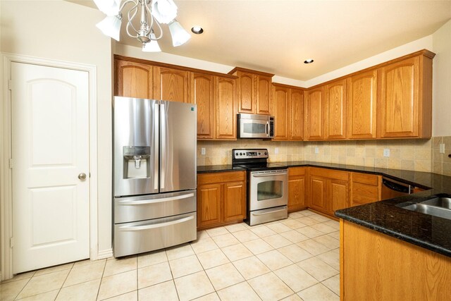 kitchen with backsplash, dark stone countertops, light tile patterned floors, stainless steel appliances, and a chandelier