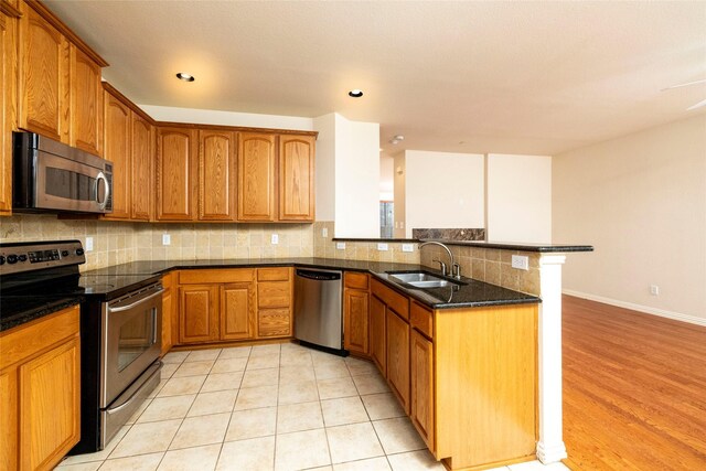 kitchen featuring sink, stainless steel appliances, kitchen peninsula, dark stone countertops, and light tile patterned floors