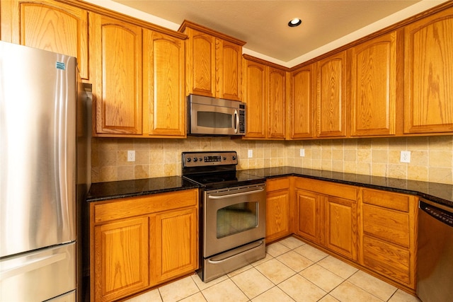 kitchen featuring backsplash, dark stone countertops, light tile patterned floors, and appliances with stainless steel finishes