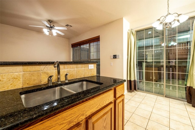 kitchen with sink, dark stone countertops, decorative light fixtures, light tile patterned floors, and ceiling fan with notable chandelier