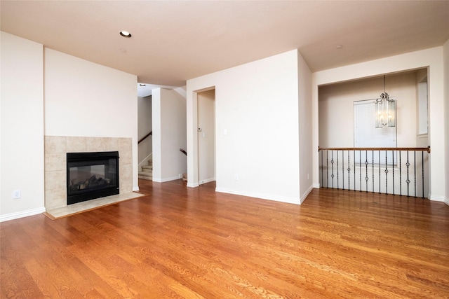 unfurnished living room featuring a tiled fireplace, an inviting chandelier, and hardwood / wood-style flooring