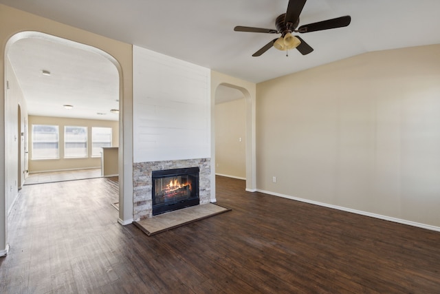 unfurnished living room with vaulted ceiling, a stone fireplace, dark hardwood / wood-style floors, and ceiling fan