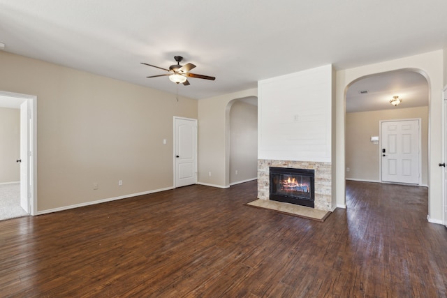 unfurnished living room with dark hardwood / wood-style flooring, a stone fireplace, and ceiling fan