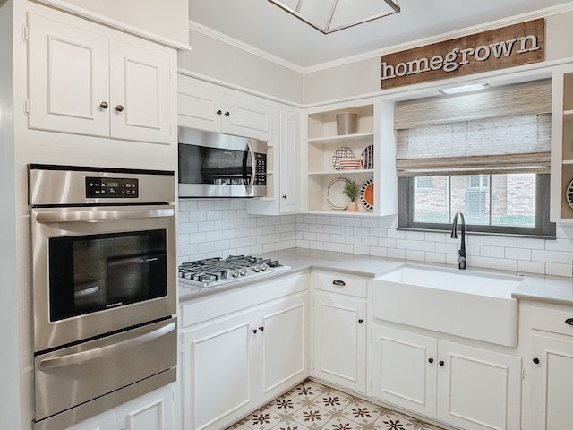 kitchen with white cabinetry, sink, stainless steel appliances, decorative backsplash, and ornamental molding