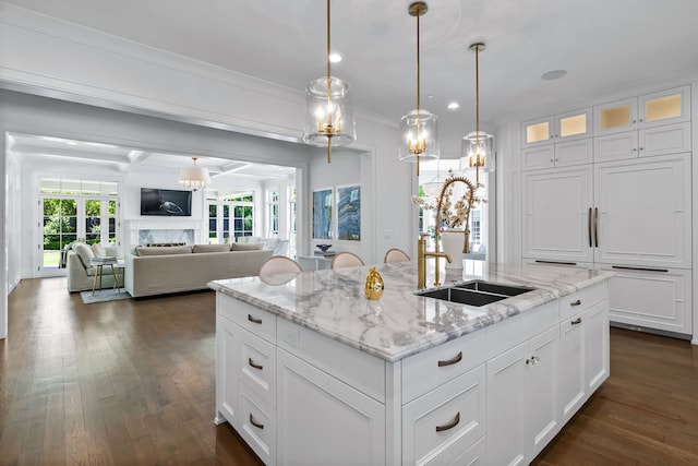 kitchen with a center island with sink, white cabinets, light stone counters, and decorative light fixtures