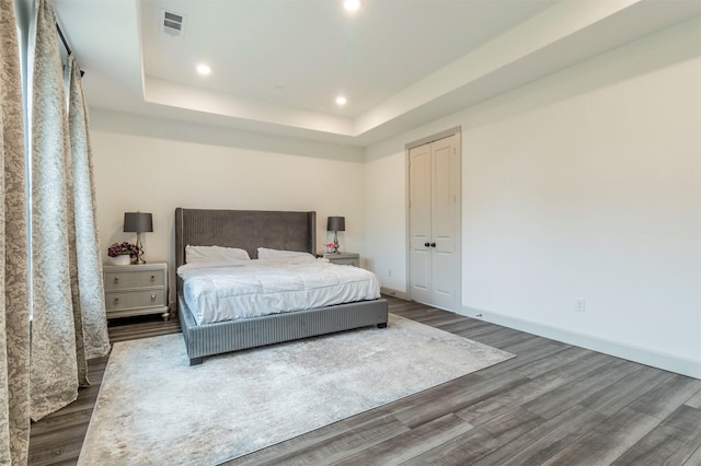 bedroom with a tray ceiling, a closet, and dark hardwood / wood-style flooring