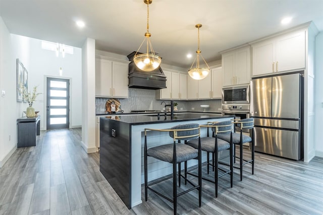 kitchen with hanging light fixtures, hardwood / wood-style flooring, an island with sink, appliances with stainless steel finishes, and white cabinetry