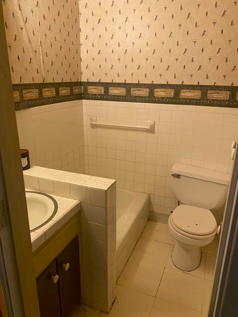 bathroom featuring vanity, a bathing tub, tile patterned floors, toilet, and tile walls