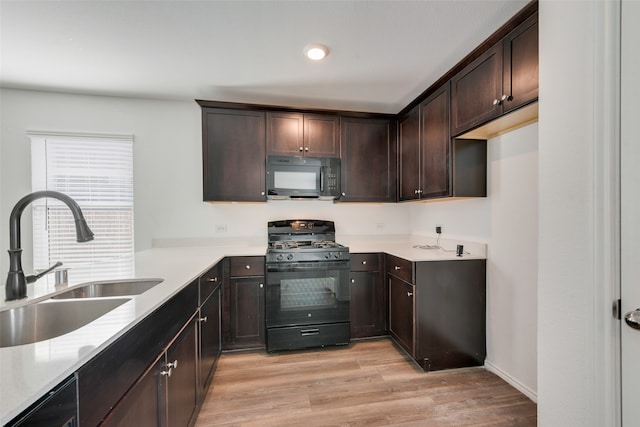 kitchen with black appliances, dark brown cabinetry, light wood-type flooring, and sink