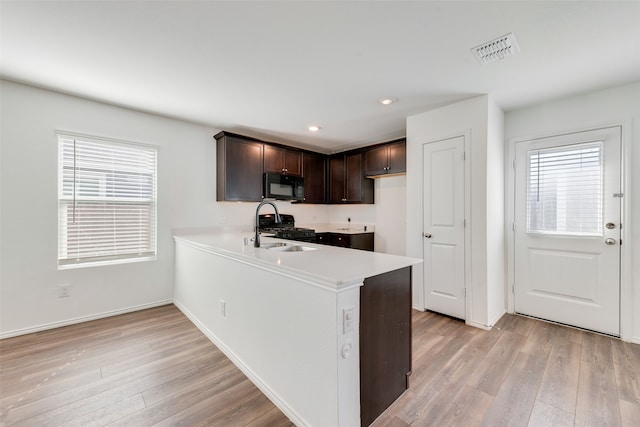 kitchen featuring black appliances, dark brown cabinets, kitchen peninsula, and light hardwood / wood-style flooring