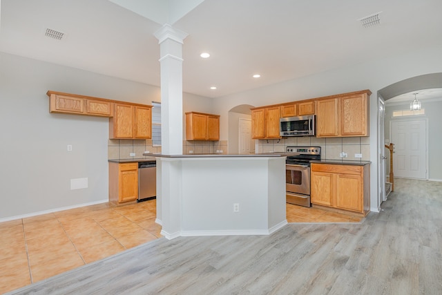 kitchen with appliances with stainless steel finishes, decorative columns, light hardwood / wood-style floors, a kitchen island, and decorative backsplash