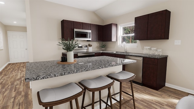 kitchen featuring a kitchen bar, dark brown cabinetry, appliances with stainless steel finishes, and vaulted ceiling