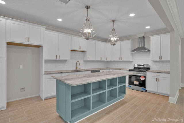 kitchen with sink, wall chimney exhaust hood, decorative light fixtures, white cabinets, and stainless steel range with gas stovetop