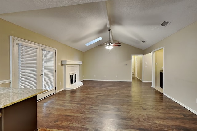 unfurnished living room featuring a textured ceiling, ceiling fan, vaulted ceiling with skylight, and dark hardwood / wood-style floors