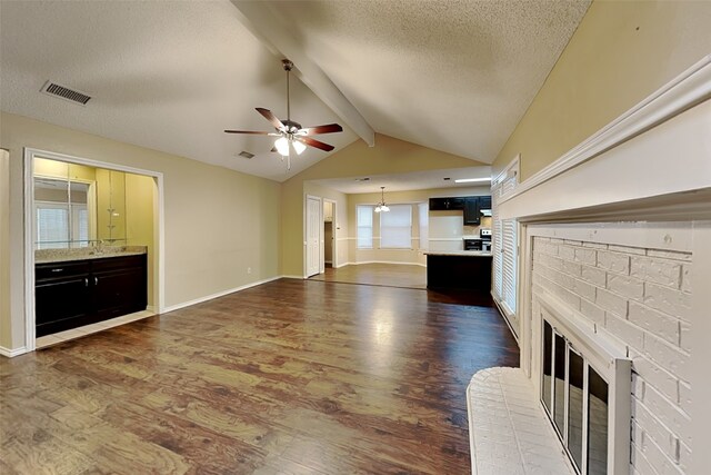 unfurnished living room featuring dark hardwood / wood-style flooring, a textured ceiling, ceiling fan, lofted ceiling with beams, and a fireplace