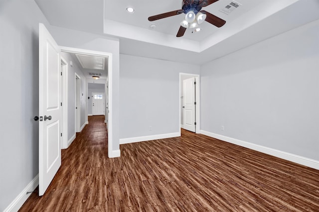 unfurnished bedroom with ceiling fan, dark wood-type flooring, and a tray ceiling