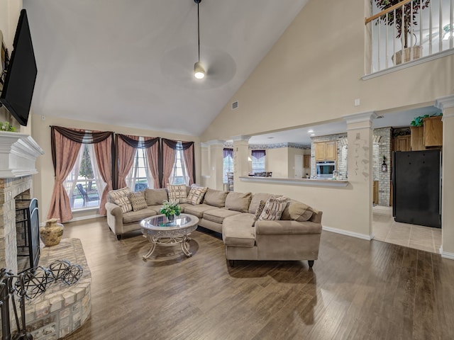 living room featuring decorative columns, ceiling fan, high vaulted ceiling, and wood-type flooring